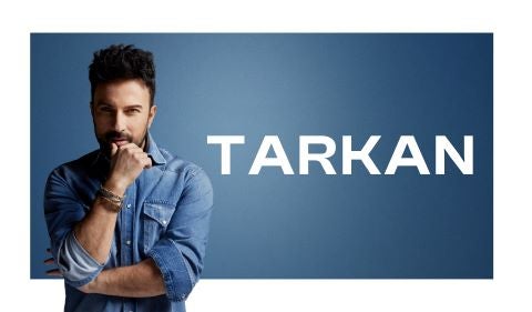 Promotional image of Tarkan against a blue background. He is wearing a denim shirt with rolled-up sleeves and bracelets on his wrist. He poses with a thoughtful expression, resting his chin on his hand. His name "TARKAN" is displayed in bold white capital letters to the right.